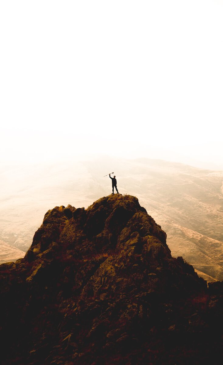 A person standing on a mountain peak at sunrise, arms raised